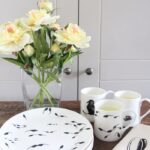 tadpoles plate in foreground with tadpoles mug and vase of flowers behind