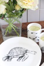 tortoise plate in foreground with tadpole mugs and vase of flowers behind