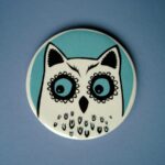 Turquoise and white ceramic owl coaster against blue background