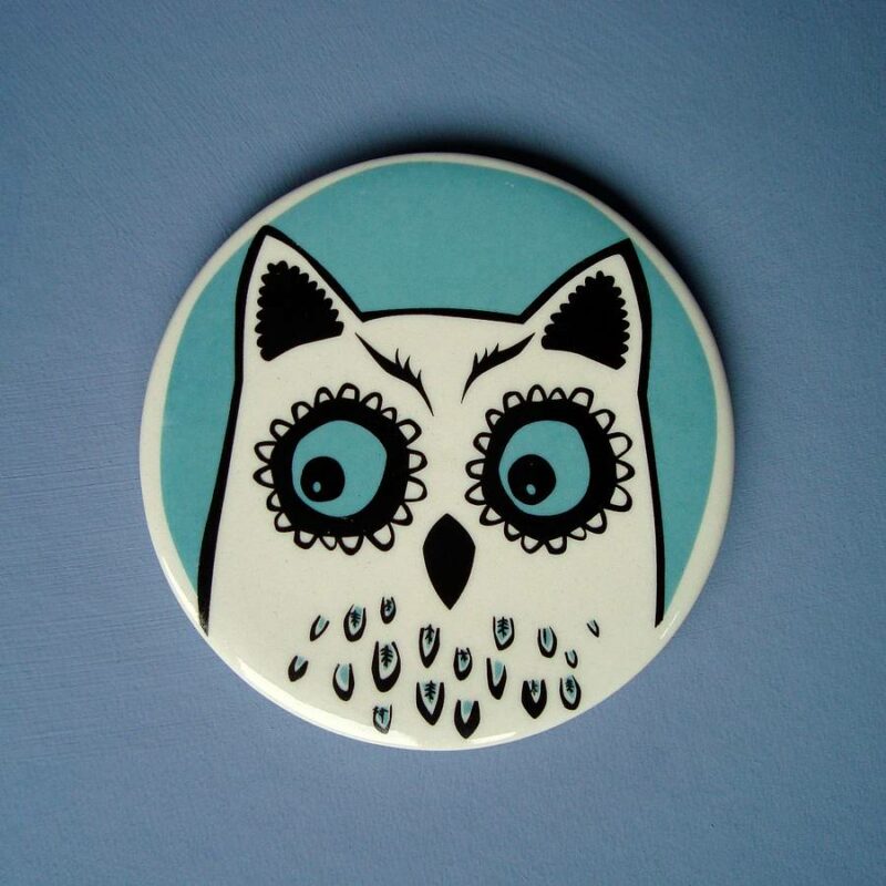 Turquoise and white ceramic owl coaster against blue background