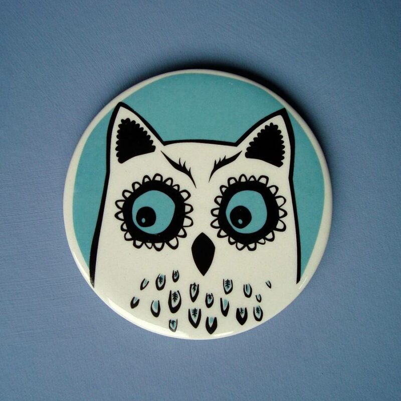 Turquoise and white ceramic owl coaster against blue background