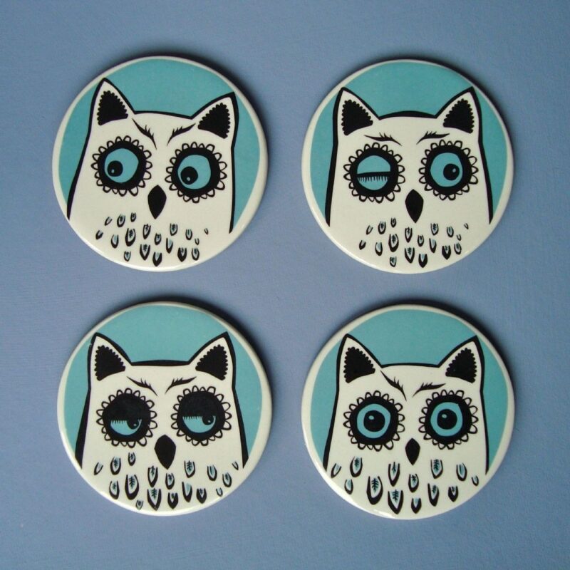 Four turquoise and white ceramic owl coasters against a blue background