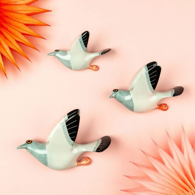 Flying pigeon trio by hannah turner seen against pink wall