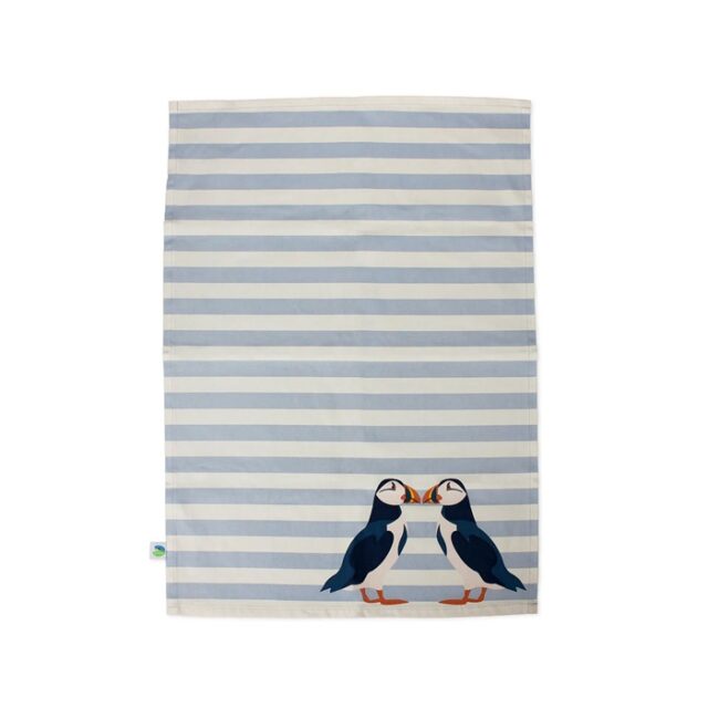 Shows the RSPB Puffin Tea Towel blue with blue and white horizontal stripes and two puffin birds facing each other with beaks touching in the right hand bottom corner