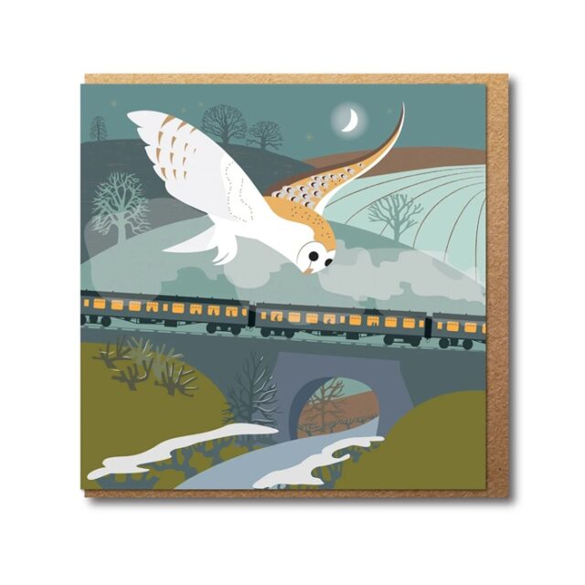 The Barn Owl and Steam Train Greetings Card by Rachel Hudson shows a white and brown owl with wings outstretched flying above a landscape with a train on a bridge going over cold ground with a river below