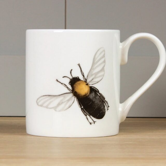 Bee mug by holly lasseter shows a black bee with golden thorax and translucent wings on a white mug