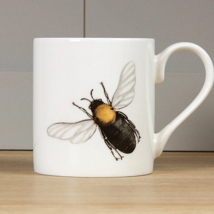 Bee mug by holly lasseter shows a black bee with golden thorax and translucent wings on a white mug