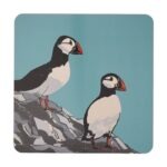 Puffins Placemat by Sue Welfare shows two black and white birds with colourful bills standing on the edge of a cliff against a blue background